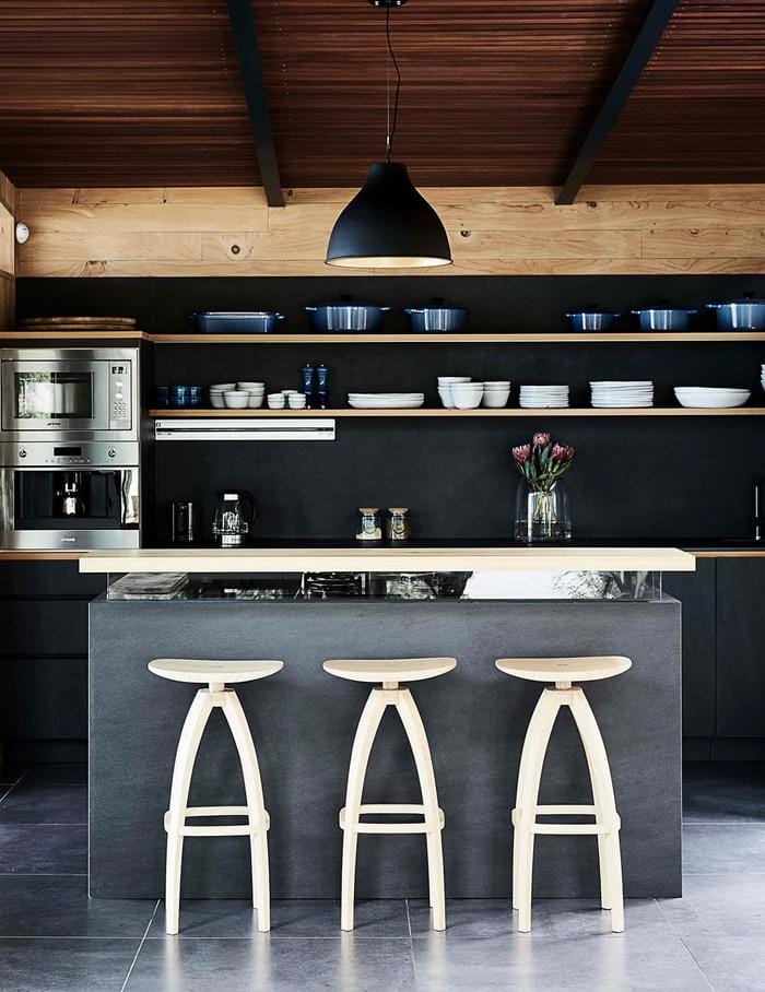 A black kitchen with wooden panelling and light wood stools
