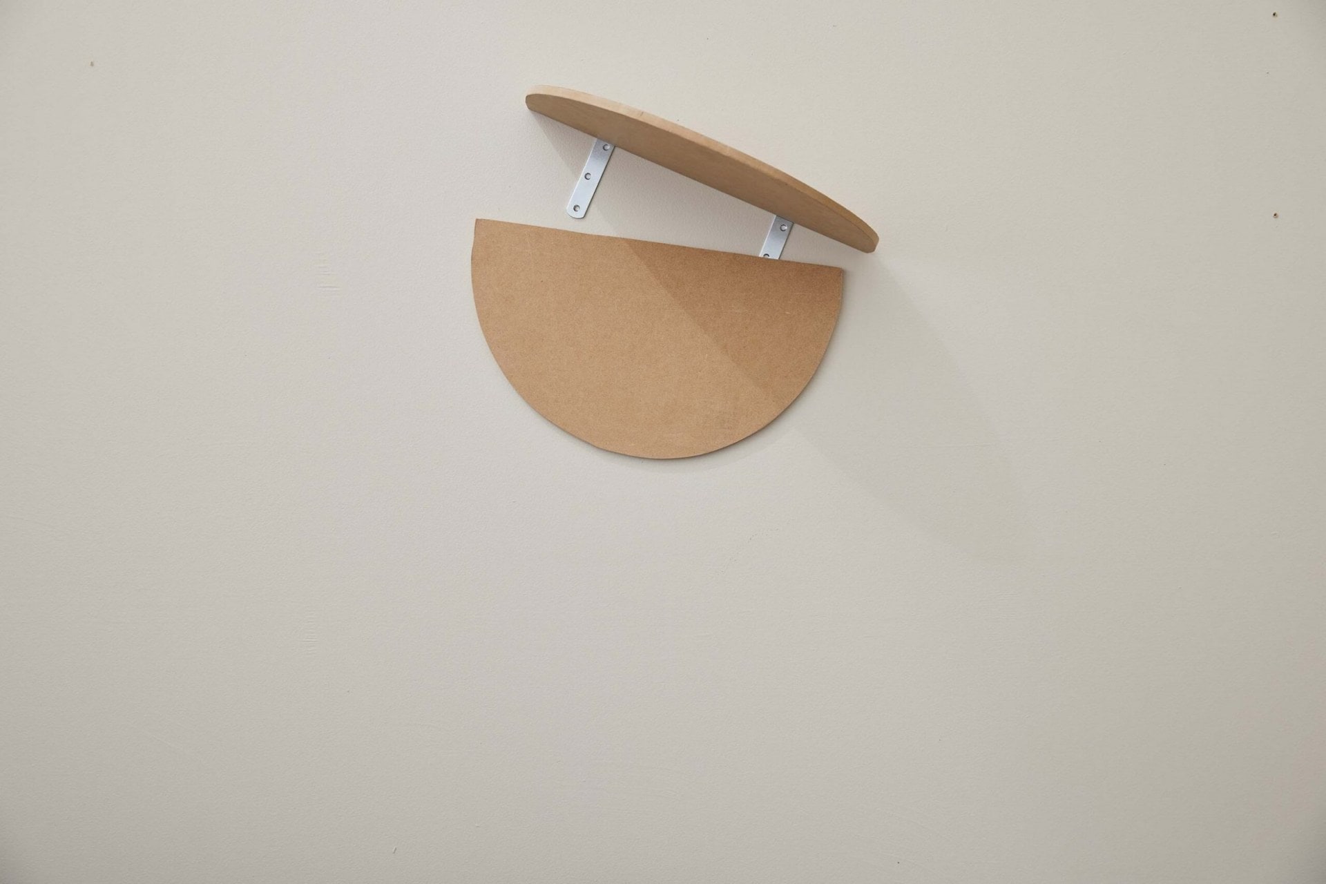 An oval MDF board hanging on wall with another piece being attached 
