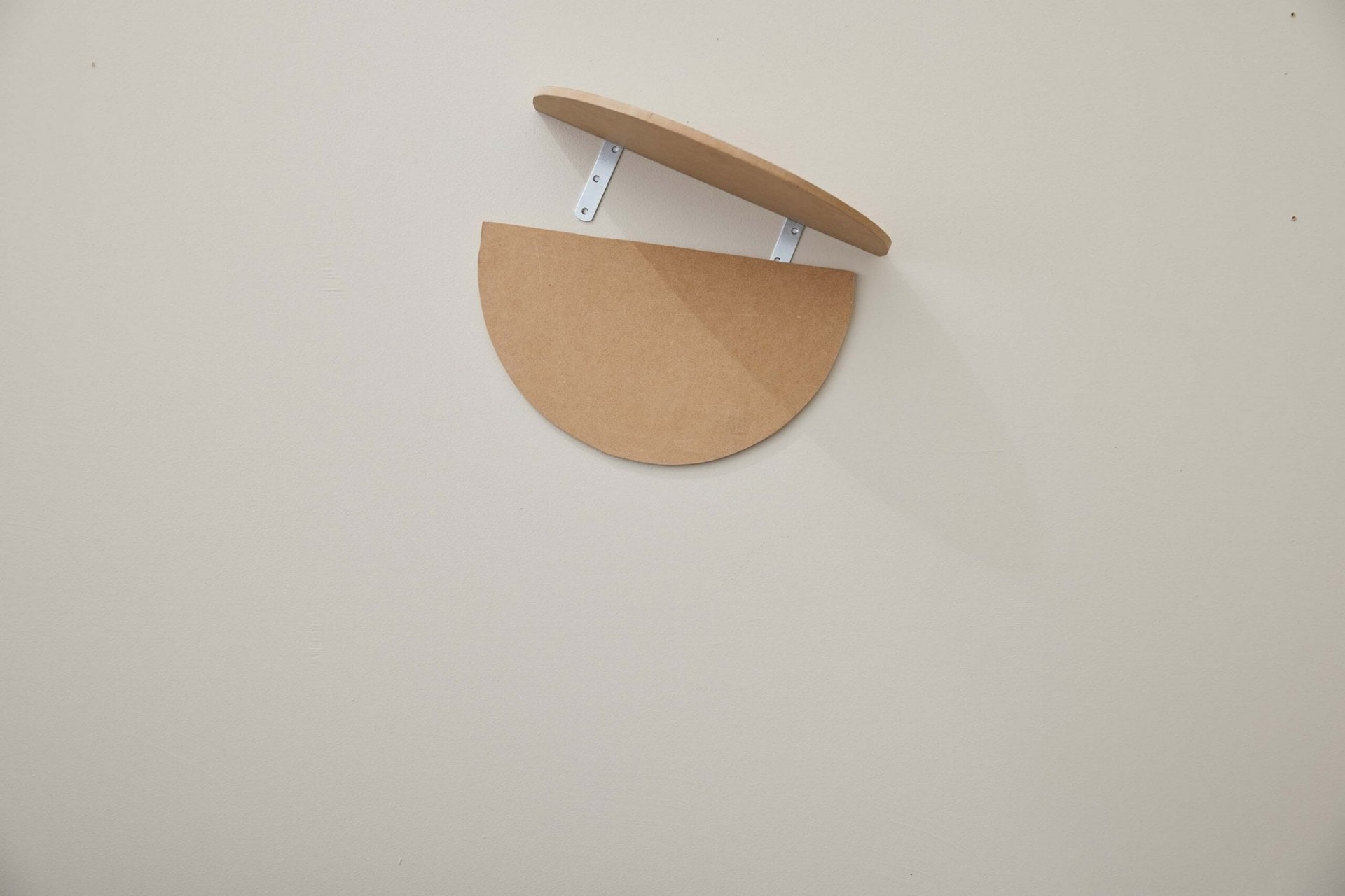 An oval MDF board hanging on wall with another piece being attached