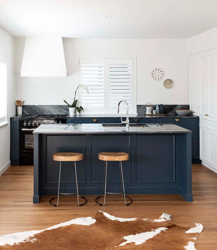 a navy blue kitchen with louvred window coverings and a sculptural extractor fan