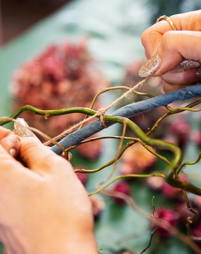 Twisted willow being tied to floral wreath hoop with brown twine