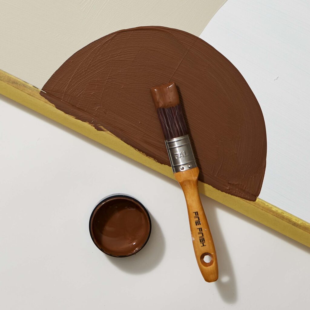 A brown Resene paint test pot and a paint brush painting an artwork