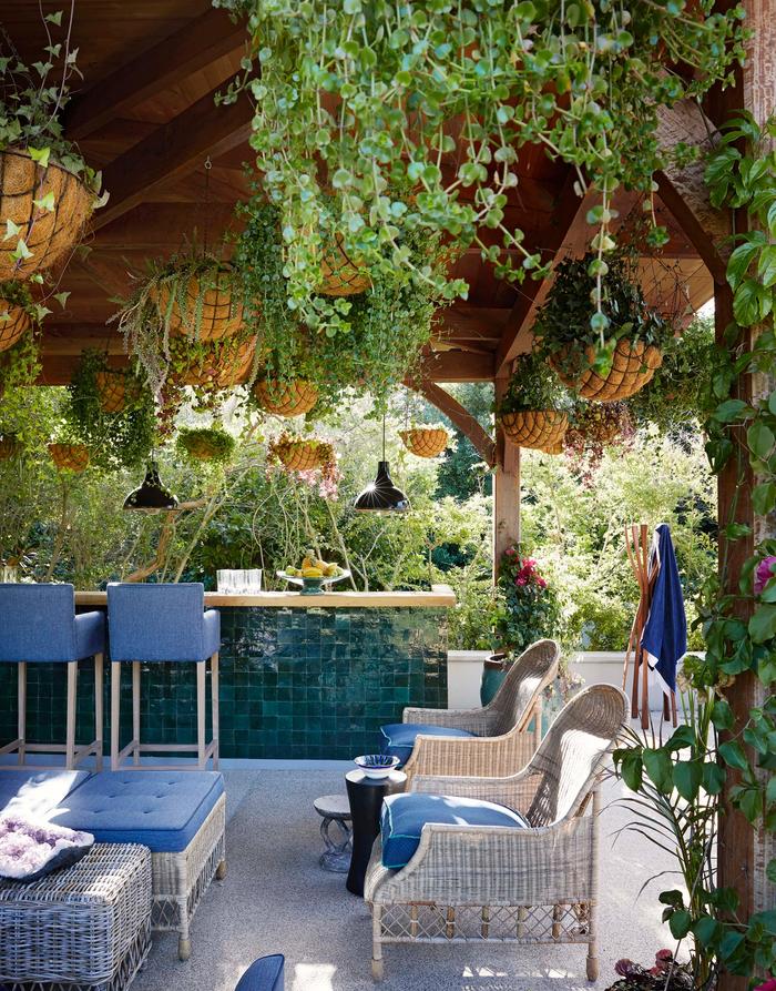 Outdoor room, with a roof with hanging plants, white wicker furniture and a bar that has green square tiles