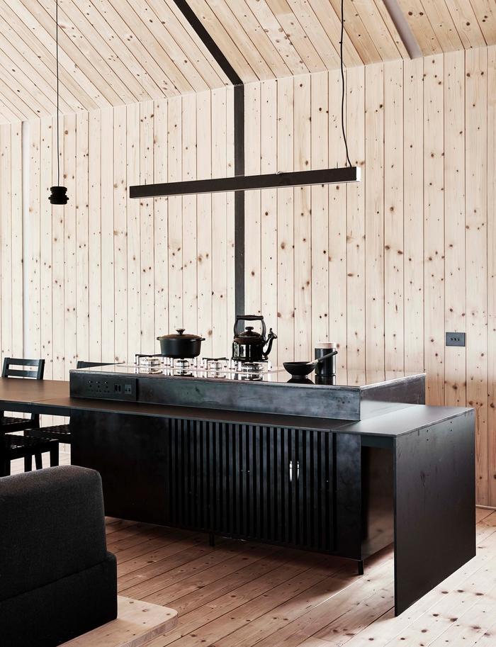 A kitchen with wood panels and floors and a dark benchtop