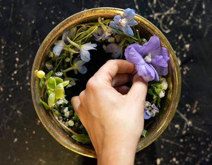 A hand placing flowers in a medium sized bowl