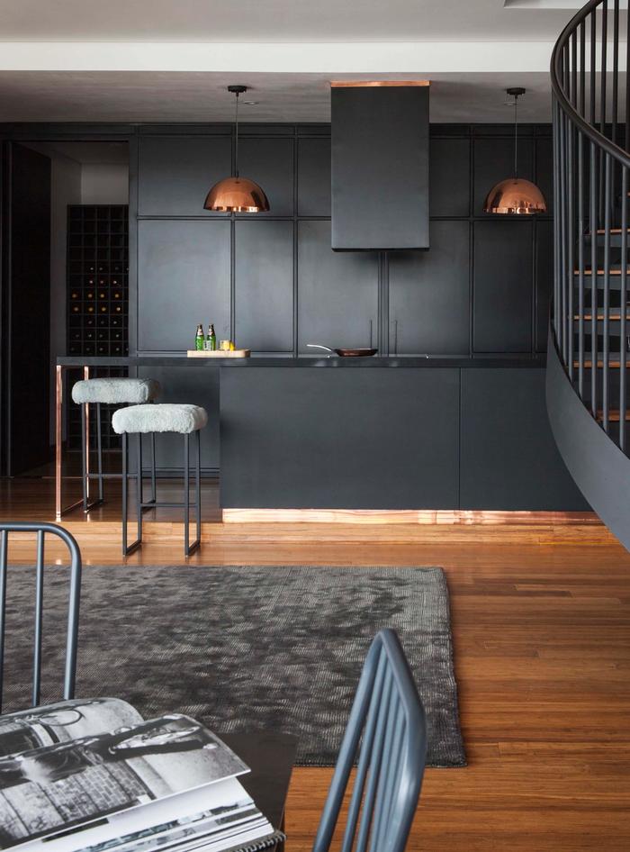 A kitchen with wood floors and brass hanging lamps and black walls and shelves