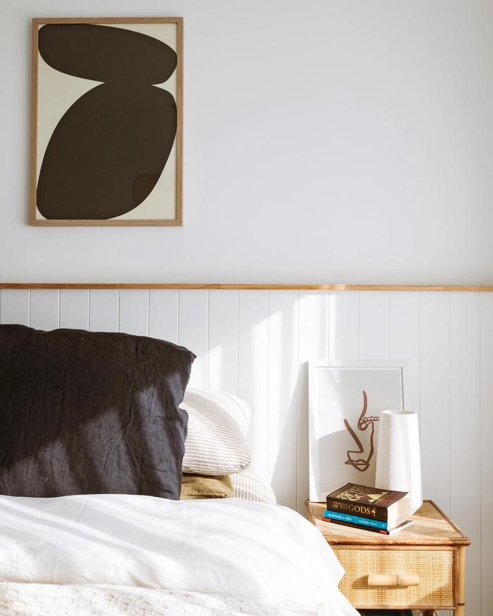 A bedroom containing a bed with a painting and wall panelling behind it.