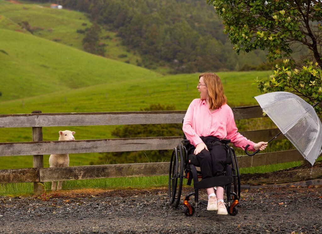 Grace Stratton holding umbrella and wearing pink top looking at sheep