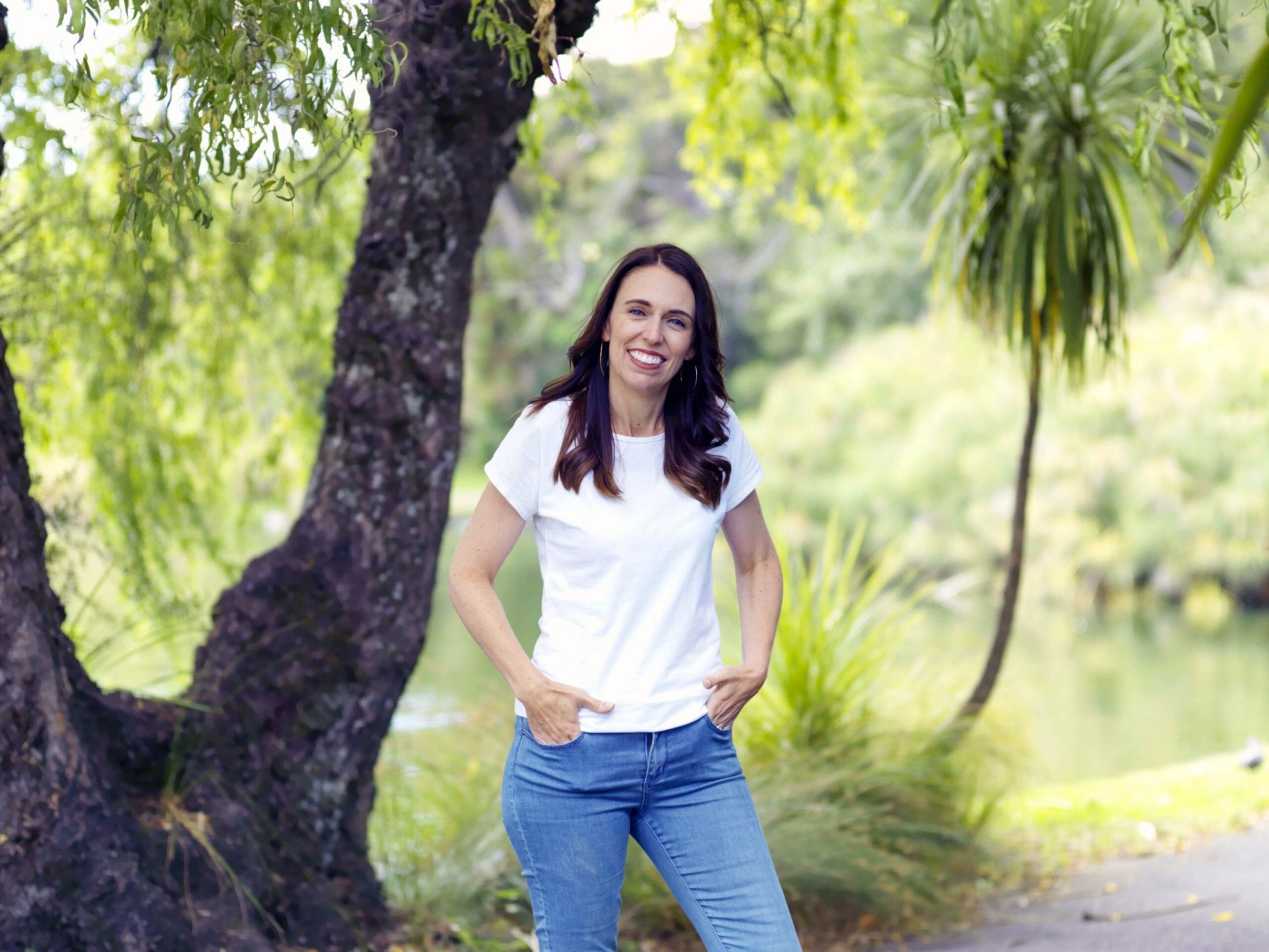 Jacinda Ardern wearing white t shirt and blue jeans standing by tree