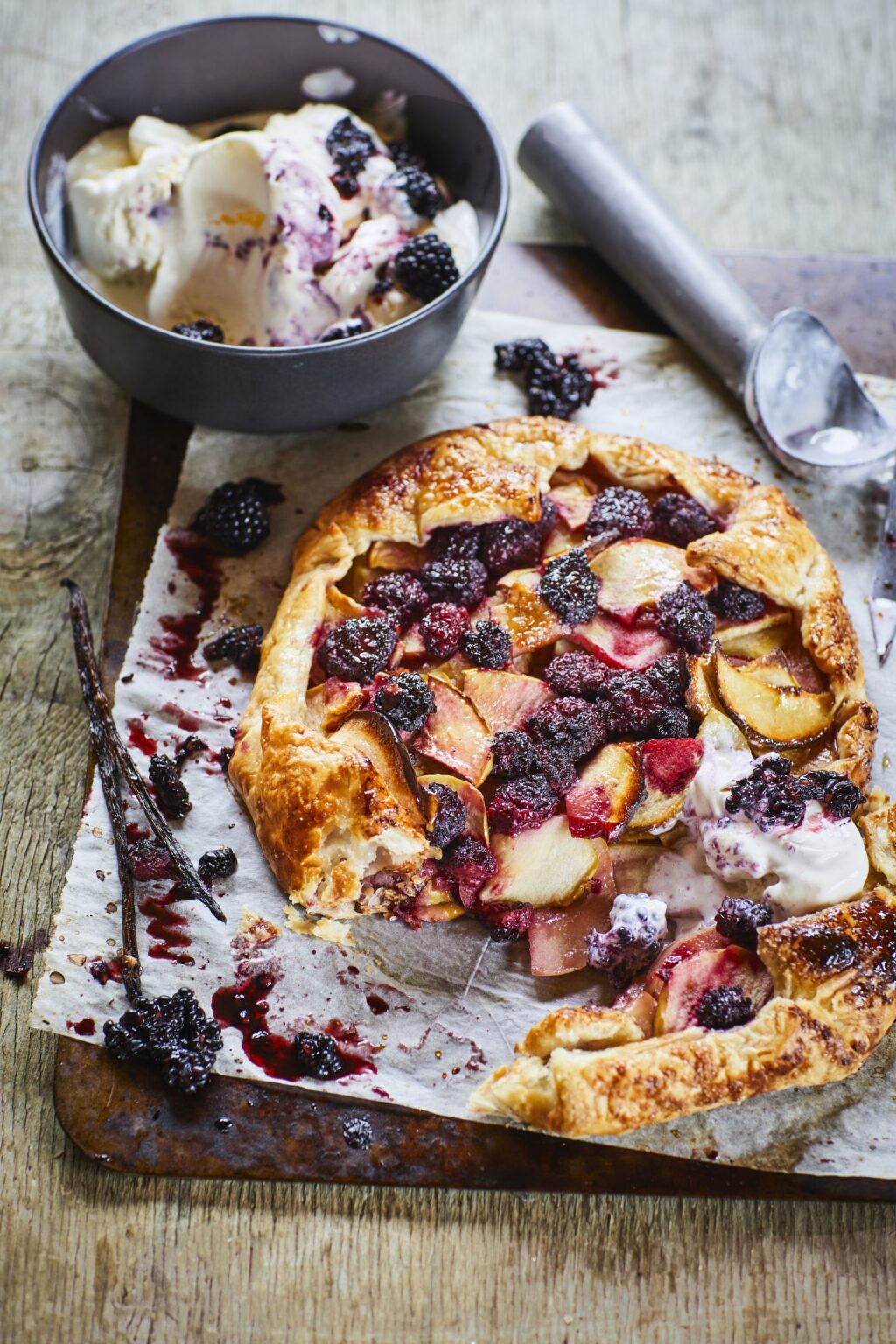 Apple, blackberry and vanilla galette on a silver baking tray next to a bowl of vanilla ice cream