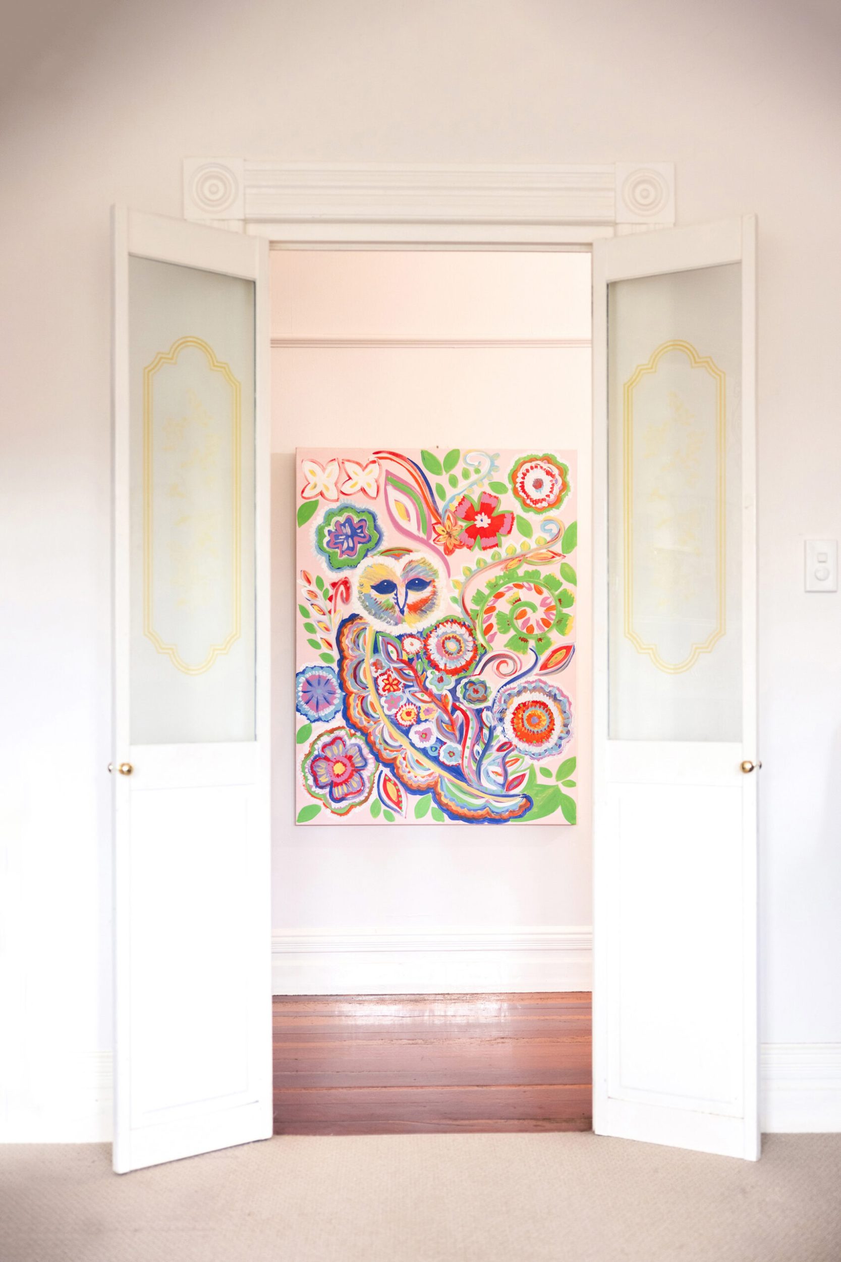 Open double doors in a tall white room showing a large colourful artwork featuring an owl