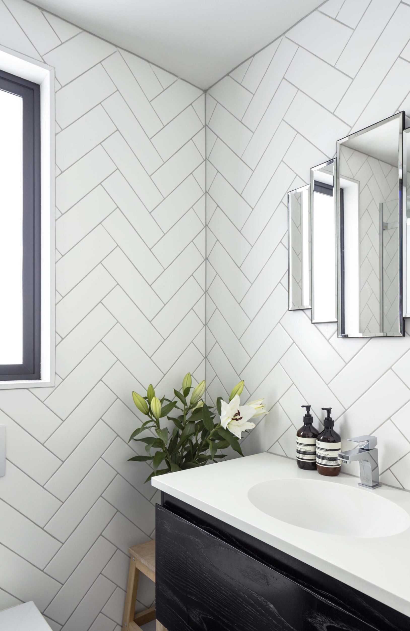 Bathroom with white diagonal subway tiles, a black vanity with a white marble top and geometric mirror