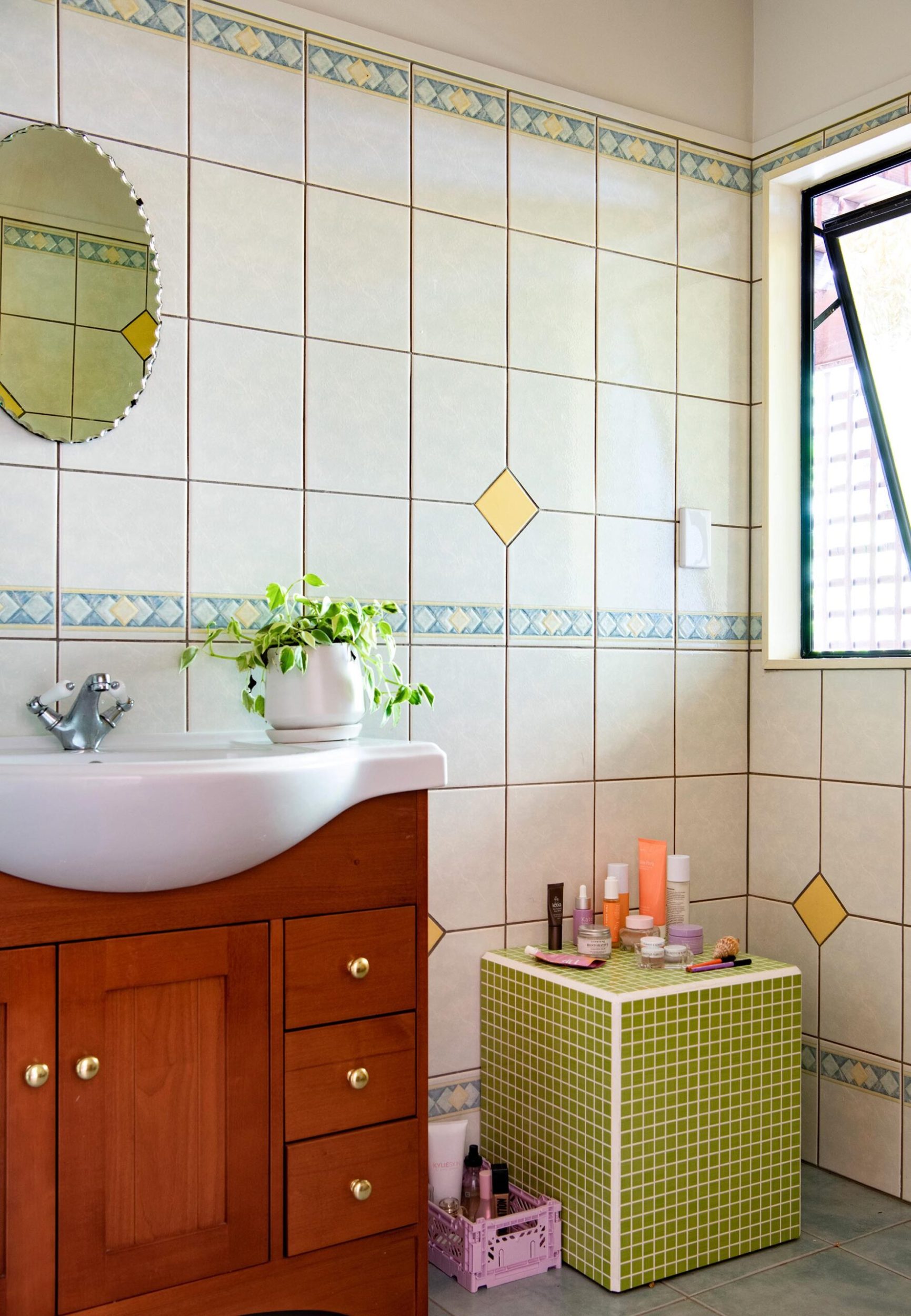 A bathroom with a wood sink cabinet, retro files and a vintage round mirror
