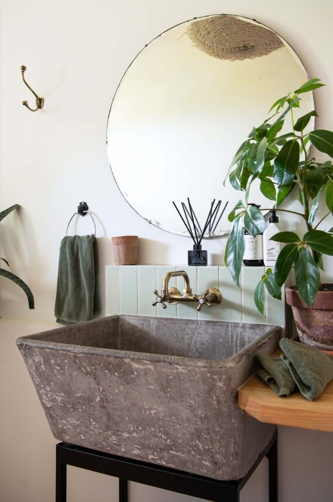 A bathroom vanity made from a concrete sink, with a round mirror hanging above