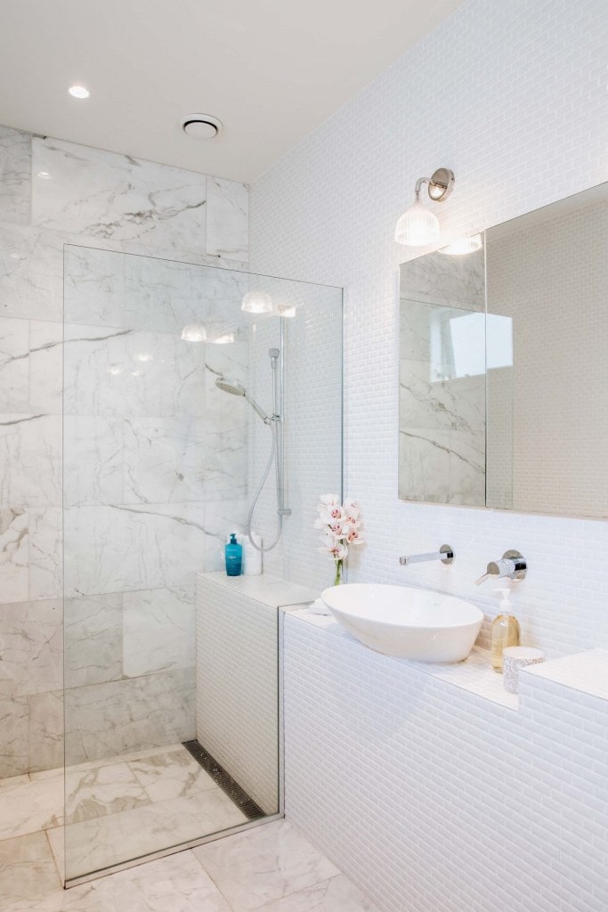 A bathroom with white and marble tiles and a clear glass divider