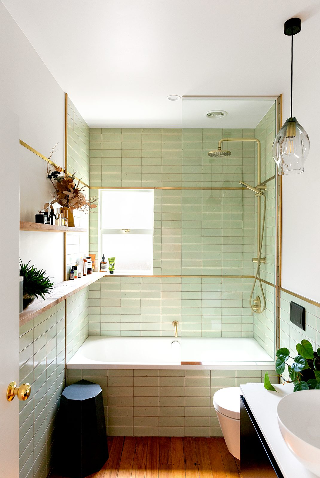 Bathroom with green tiles and hanging lights with brass and black touches