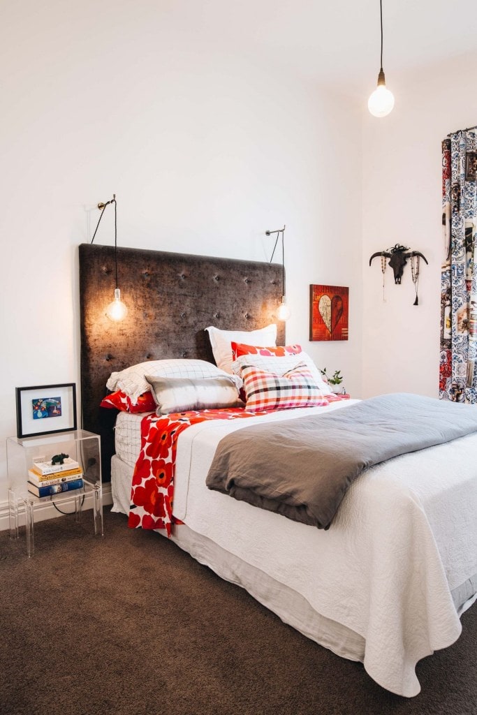 bedroom with large black furnished headboard, red and white linens, and printed curtains
