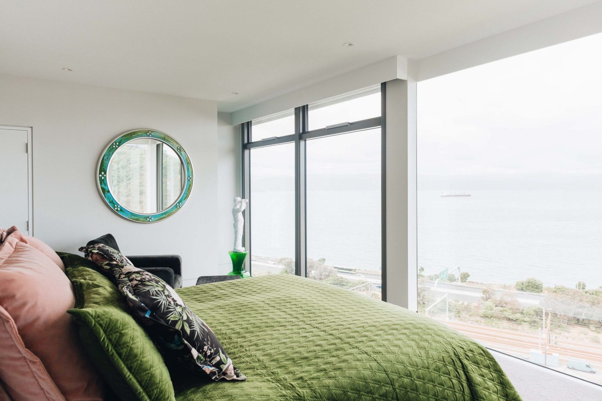 Bedroom with a moss green bed duvet and large glass windows 
