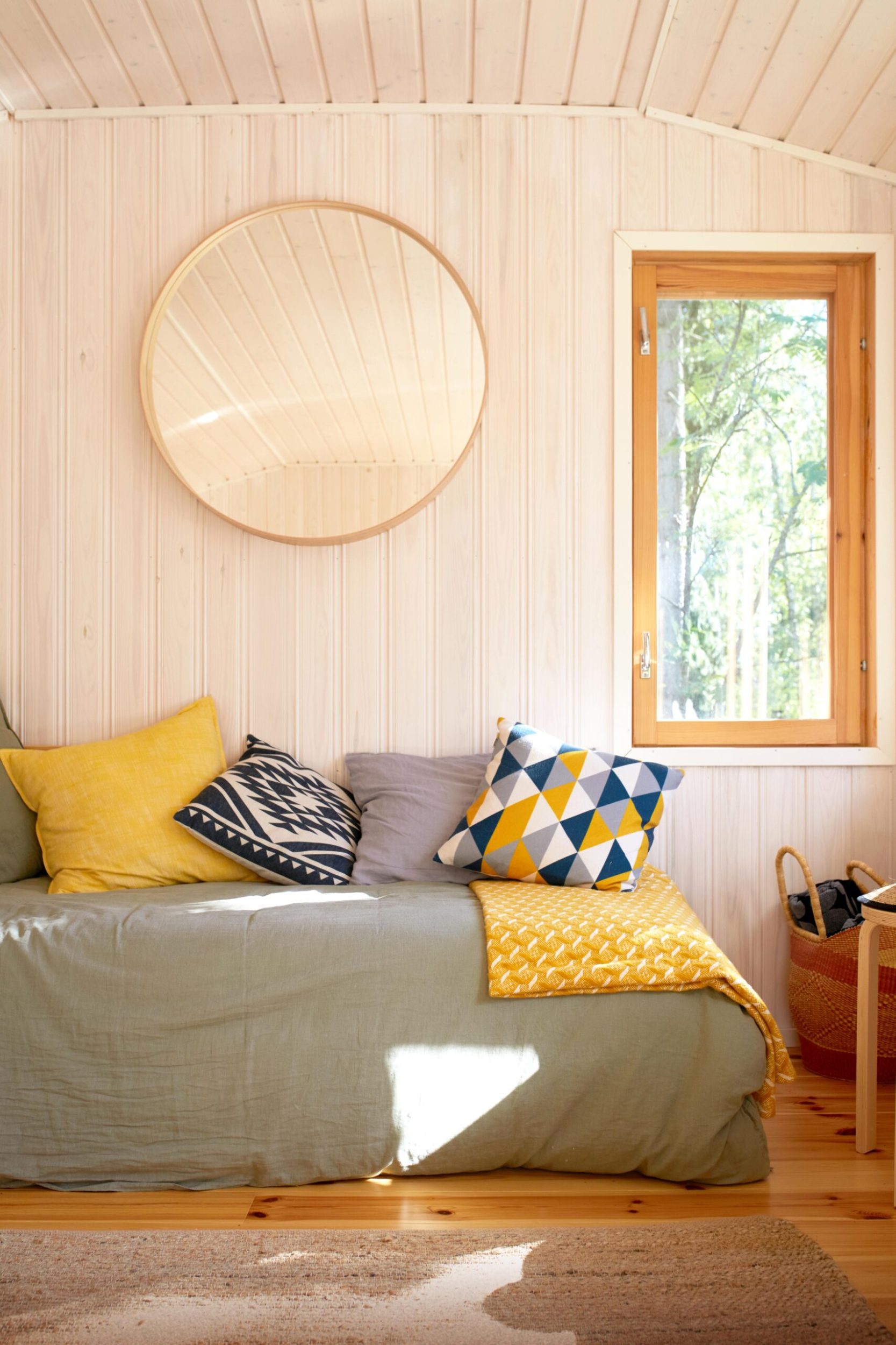 Bedroom with light wood panels, polished wood floors and a bed with grey duvet and yellow pillows 