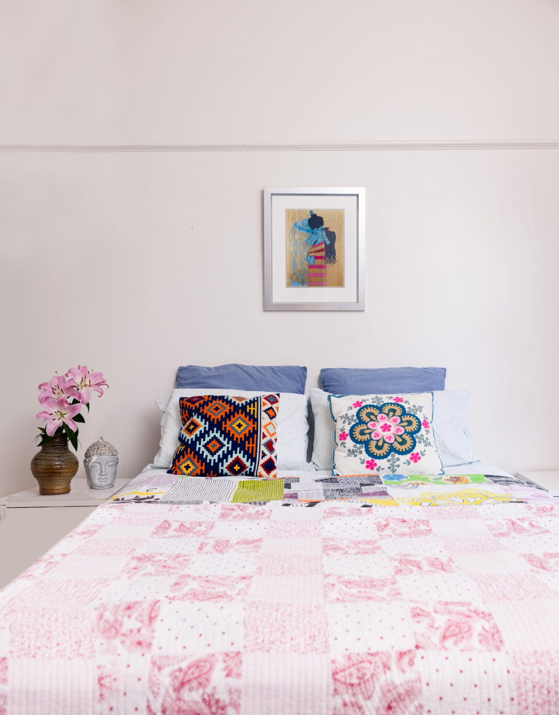 A light grey room with a double bed with pink covers and crochet cushions