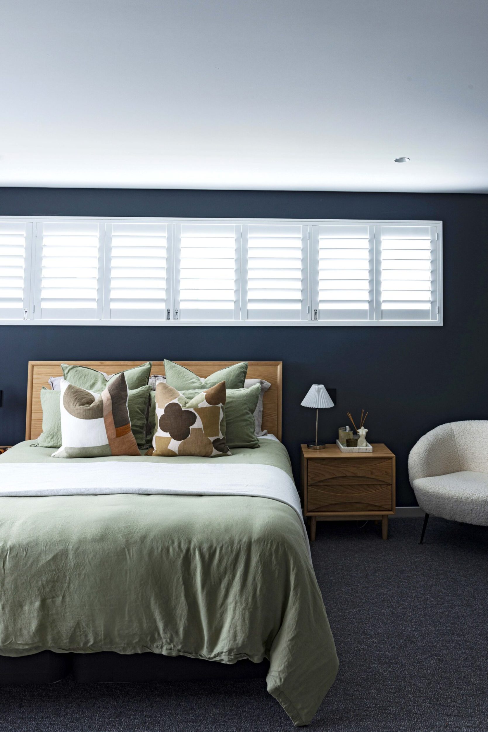 Bedroom painted in a deep blue, with shutters on the windows above the bed, and sage green coloured bed linen