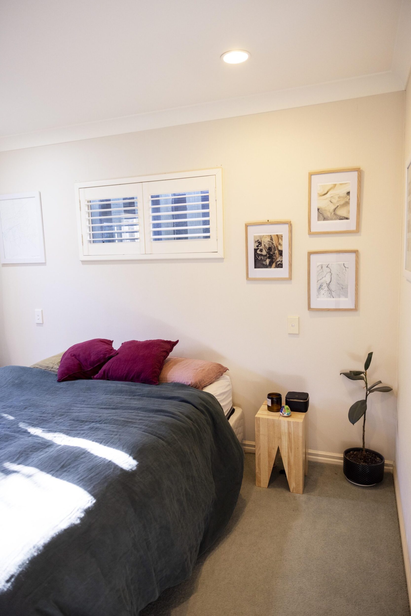 A bedroom with white walls, grey carpet and a bed with a black bedspread