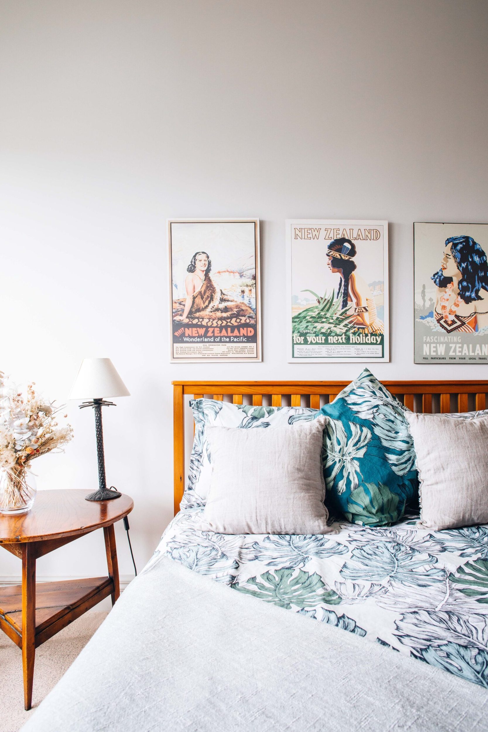 A bedroom with a Queen sized bed, a wooden side table and hanging vintage New Zealand tourism prints