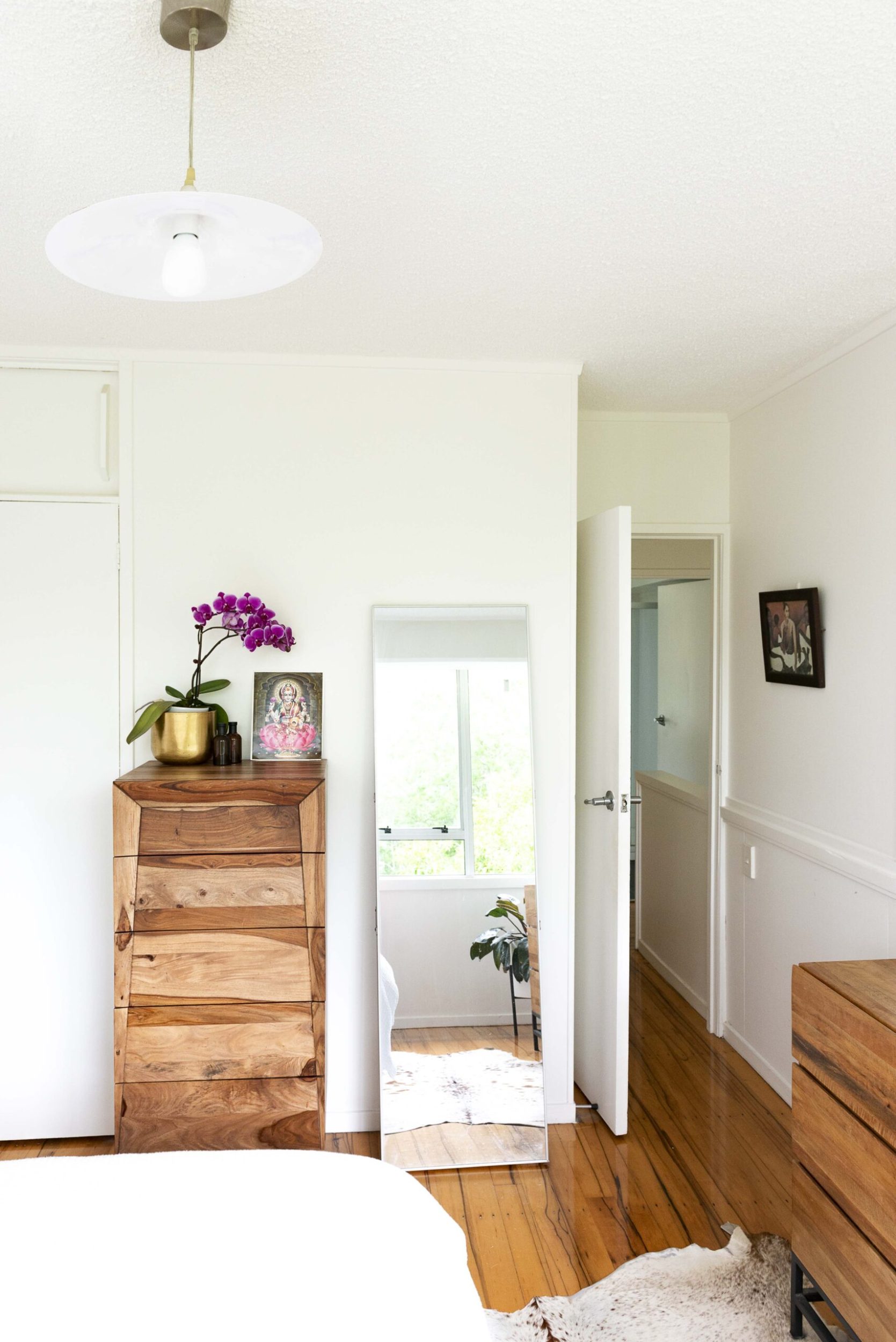 Bedroom with polished wooden floors, brown drawers and large mirror 