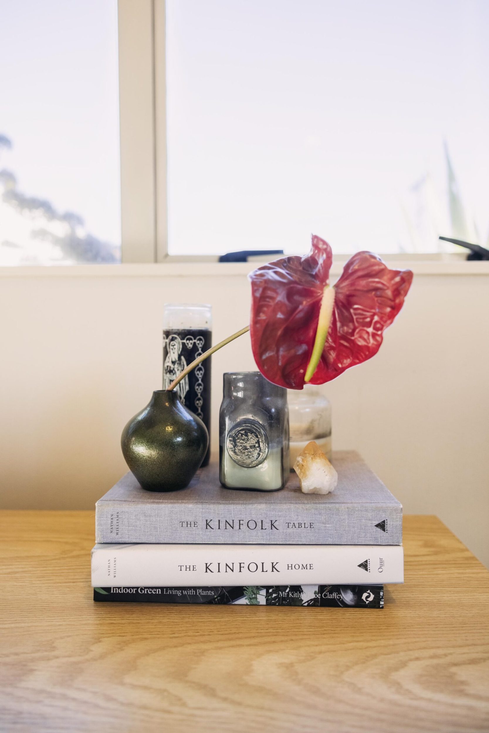 A wood bedside table with a stack of The Kinfolk books, candles and decorative red flower