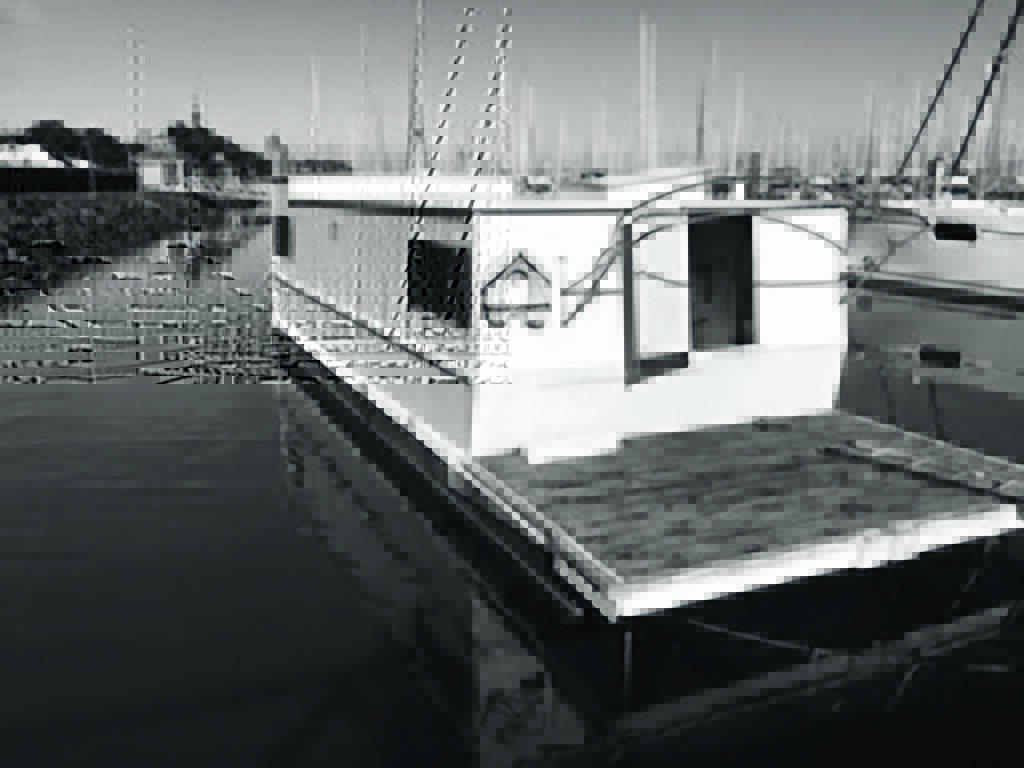 A black and white photo of a houseboat docked in a marina