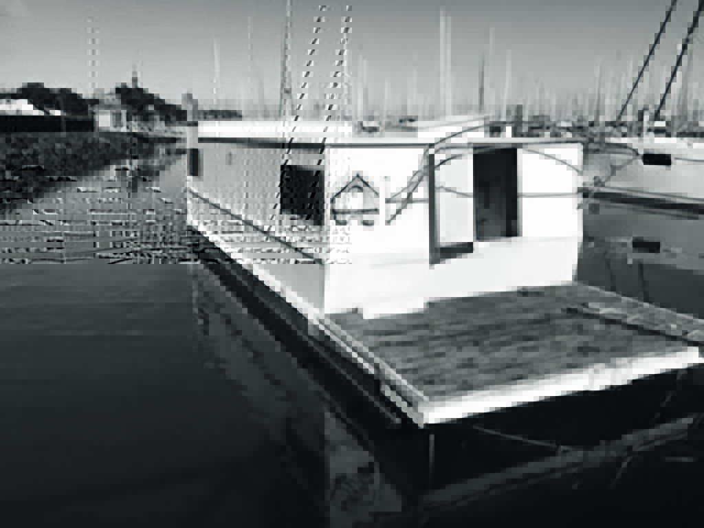 A black and white photo of a houseboat docked in a marina
