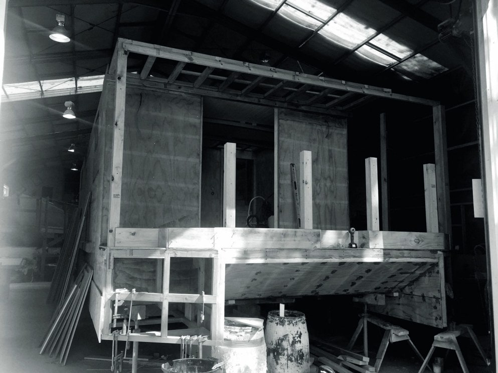 A black and white photo of a houseboat being renovated in a warehouse