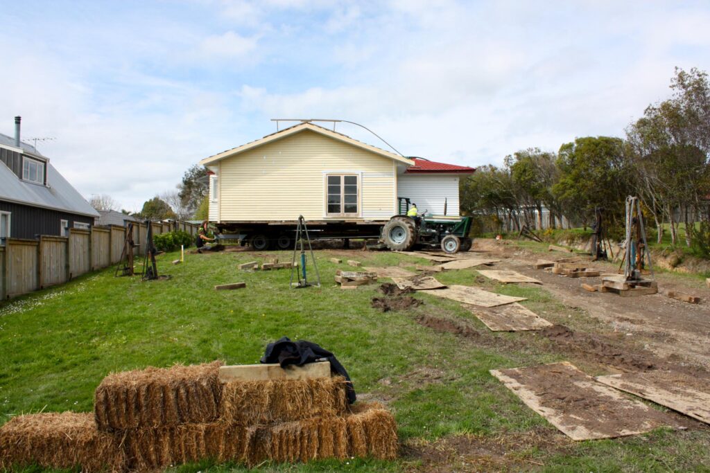 An old yellow home being relocated by a tractor