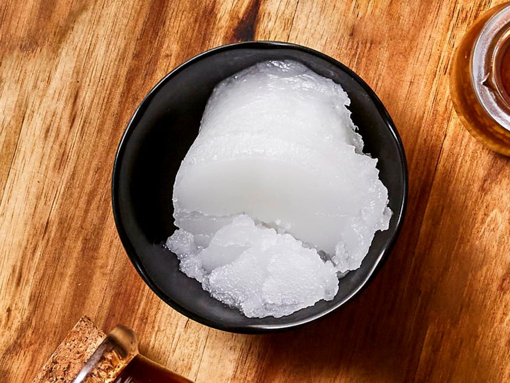 Biobalance Certified Organic Virgin Coconut Oil in a black bowl on a wood round tray