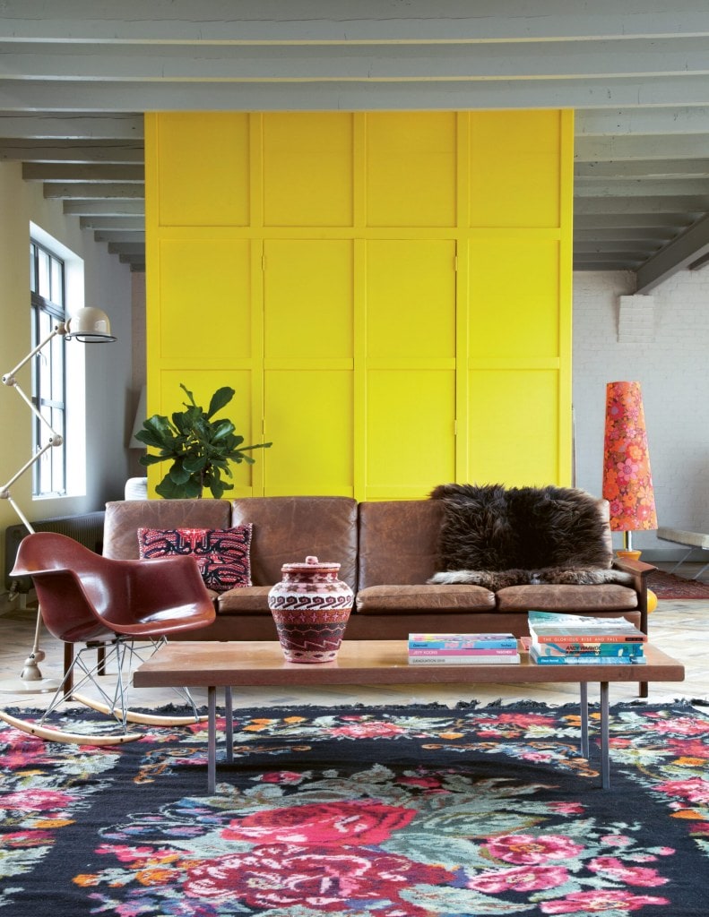 Living room with a yellow wall, patterned rug and brown couch