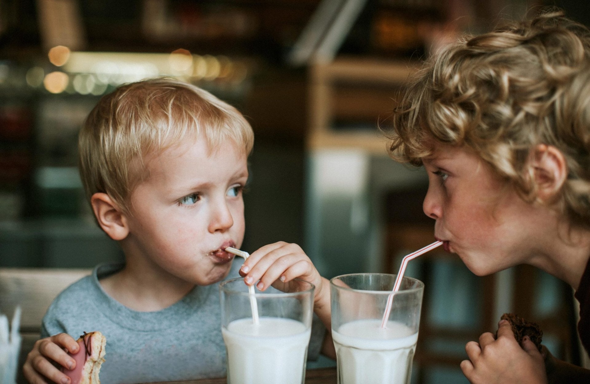 Two young boys drinking milk out of draws while sitting together 