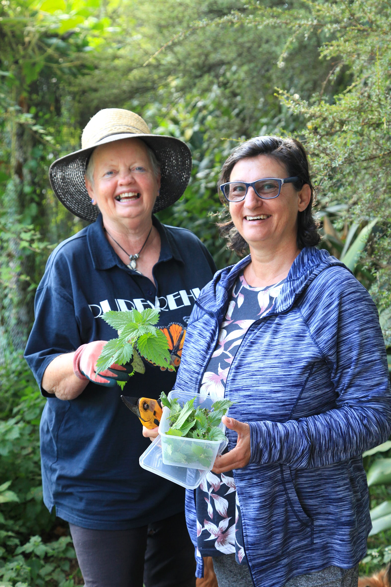 Jacqui Knight and Melody Shinnick standing in garden holding containers of plants
