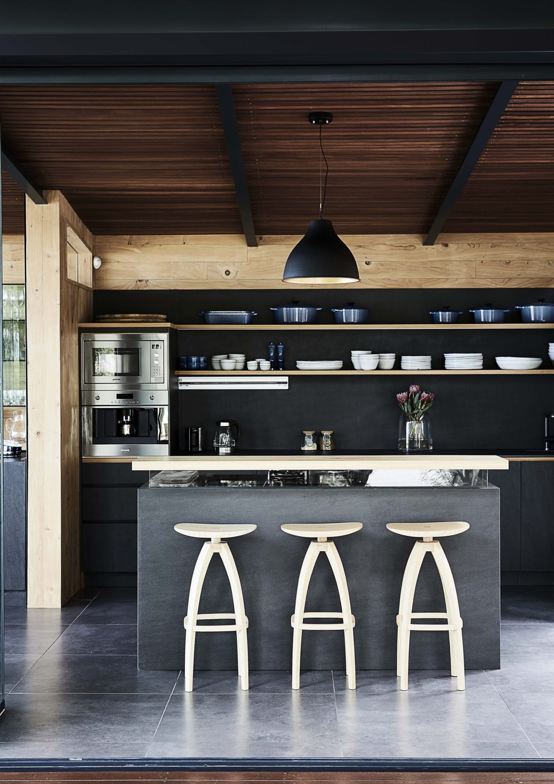 A black kitchen with wooden panelling and light wood stools