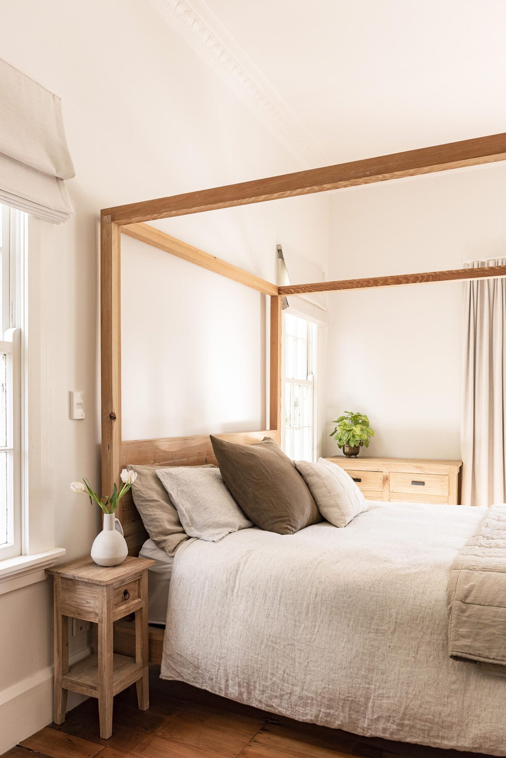 A wood canopy bed with a beige linen duvet cover and a wooden vintage side table