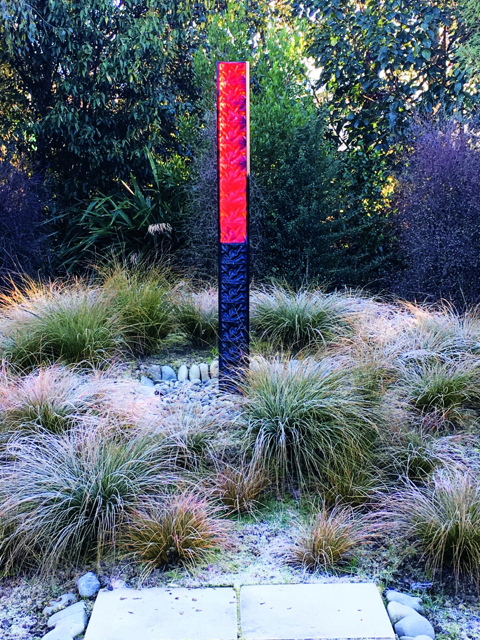 A black and red cast-glass pou totem by Jenny Smith in a garden