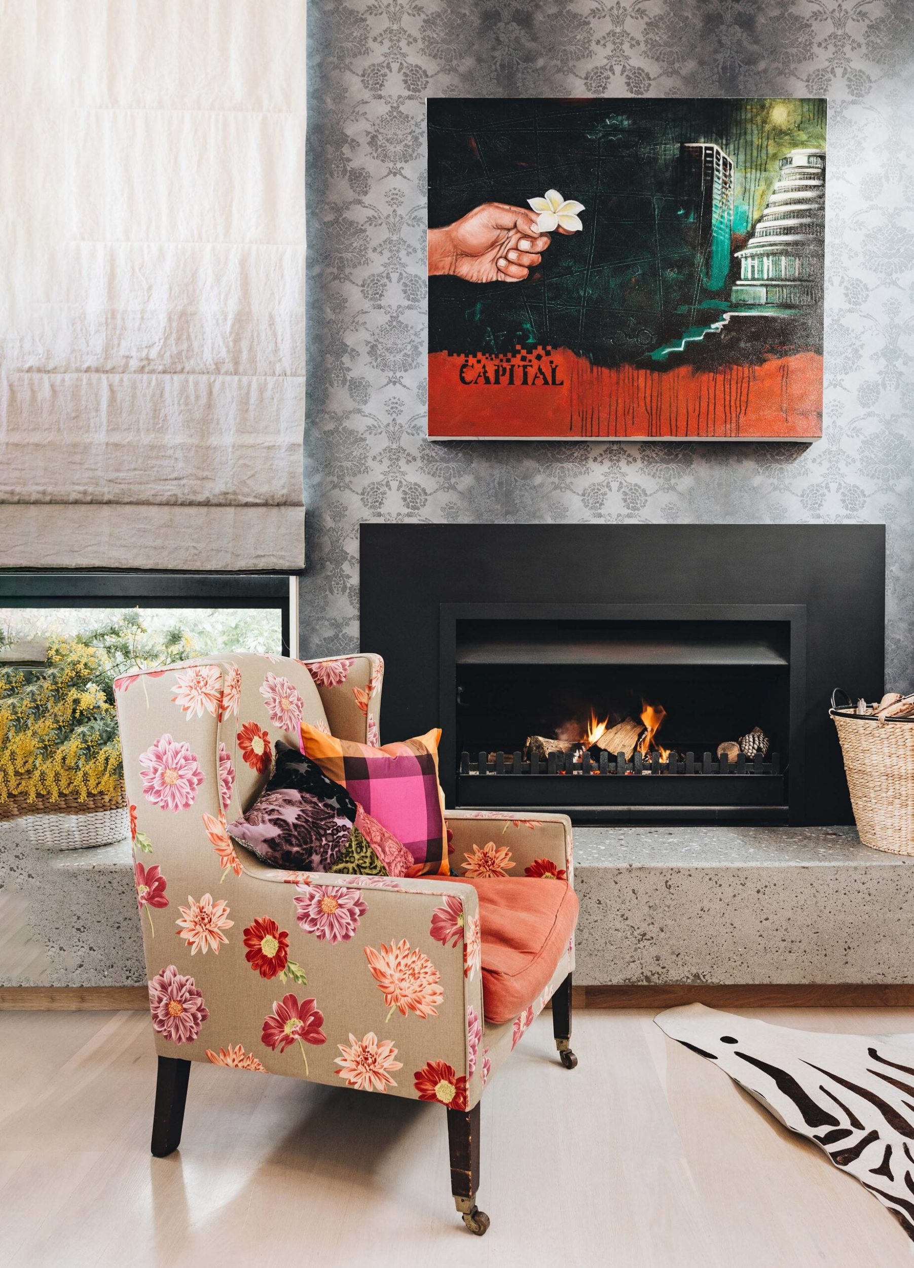 A furnished chair sitting in front of a fireplace with a David Teata painting above it