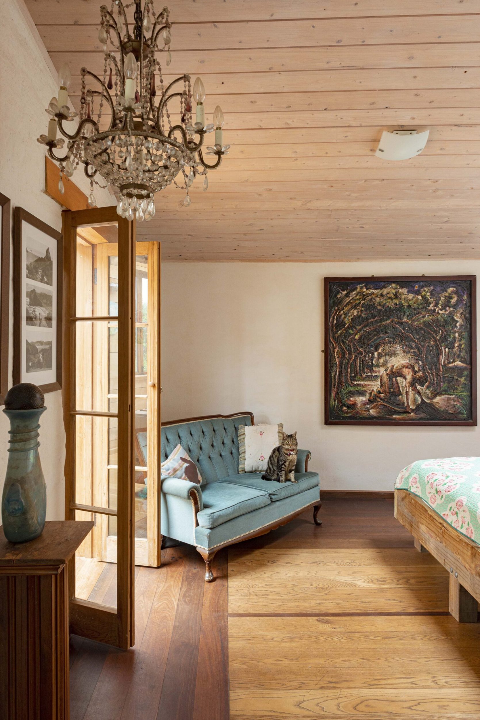 A bedroom with white walls, wood floors, a blue French chair and hanging chandelier