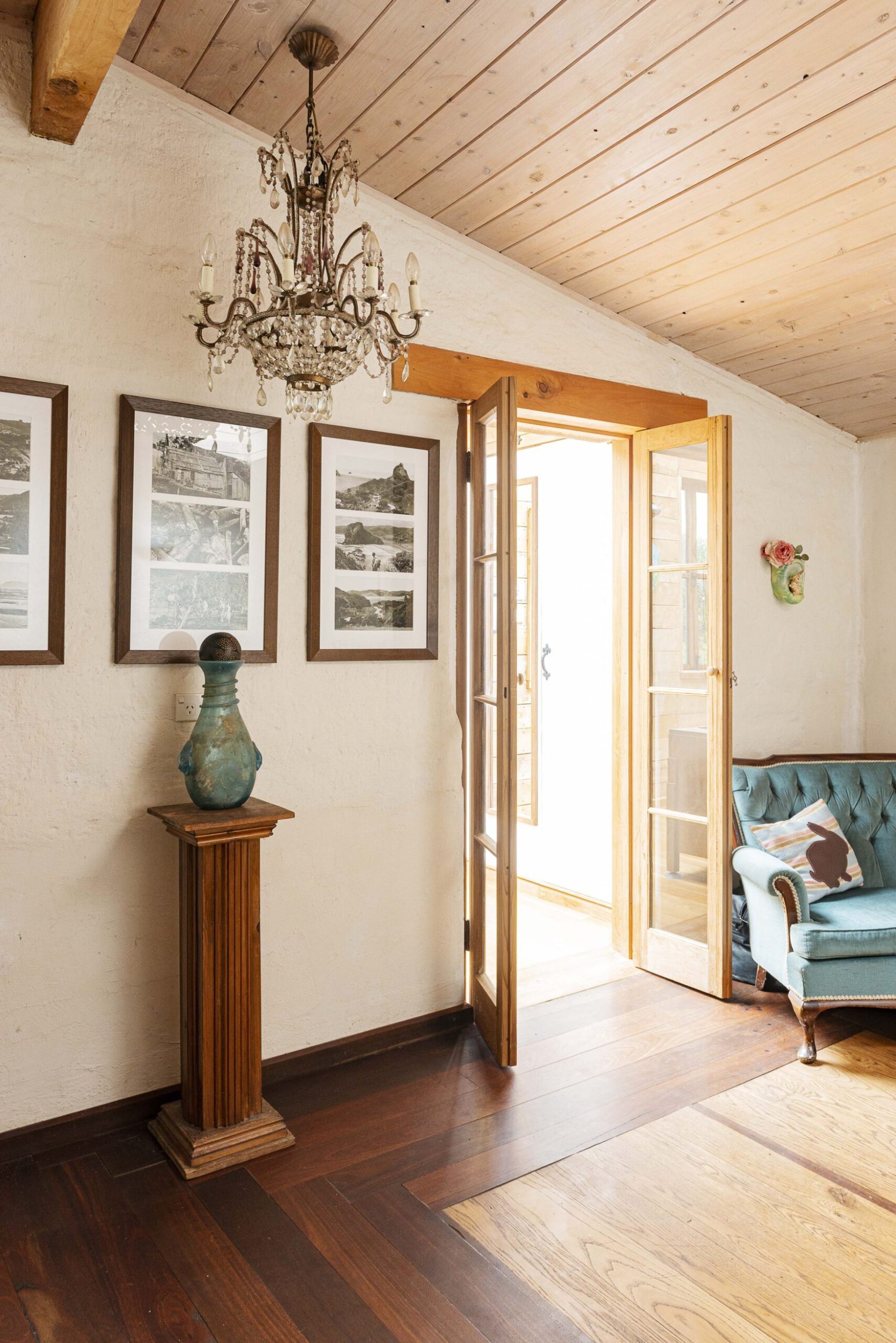 A room with dark wood floors, open wood doors, a chandelier, and a blue French couch