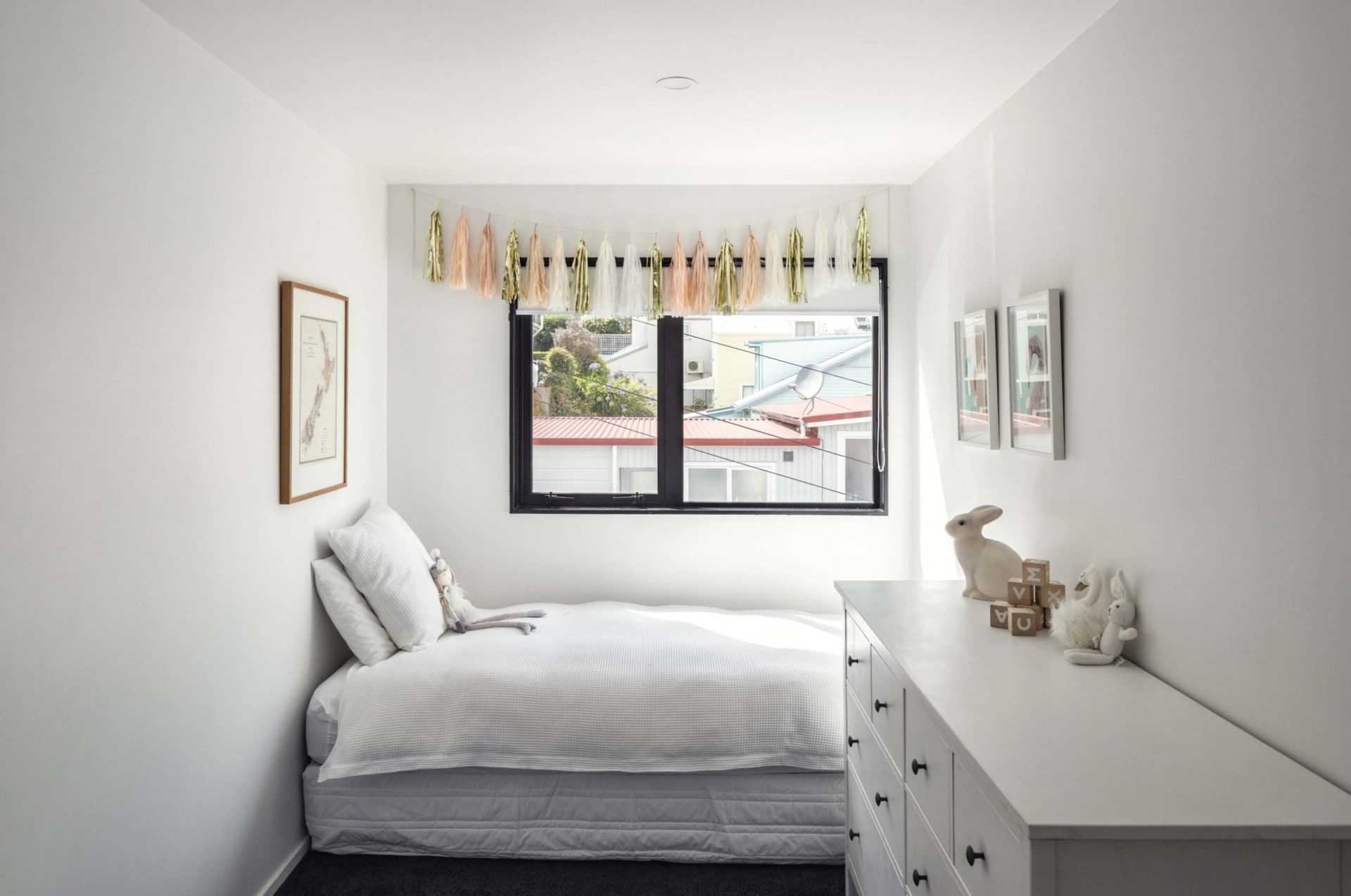 A white children's room with a window with pink, gold and white tassels 