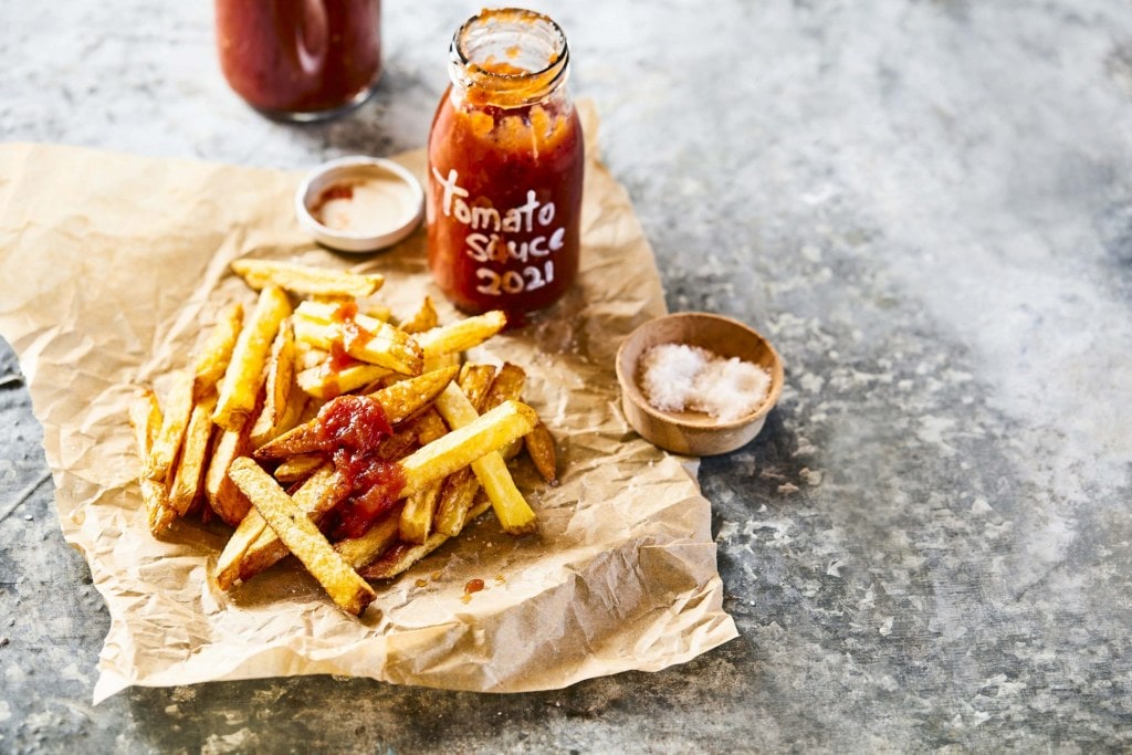 A bottle of tomato sauce surrounded by chips