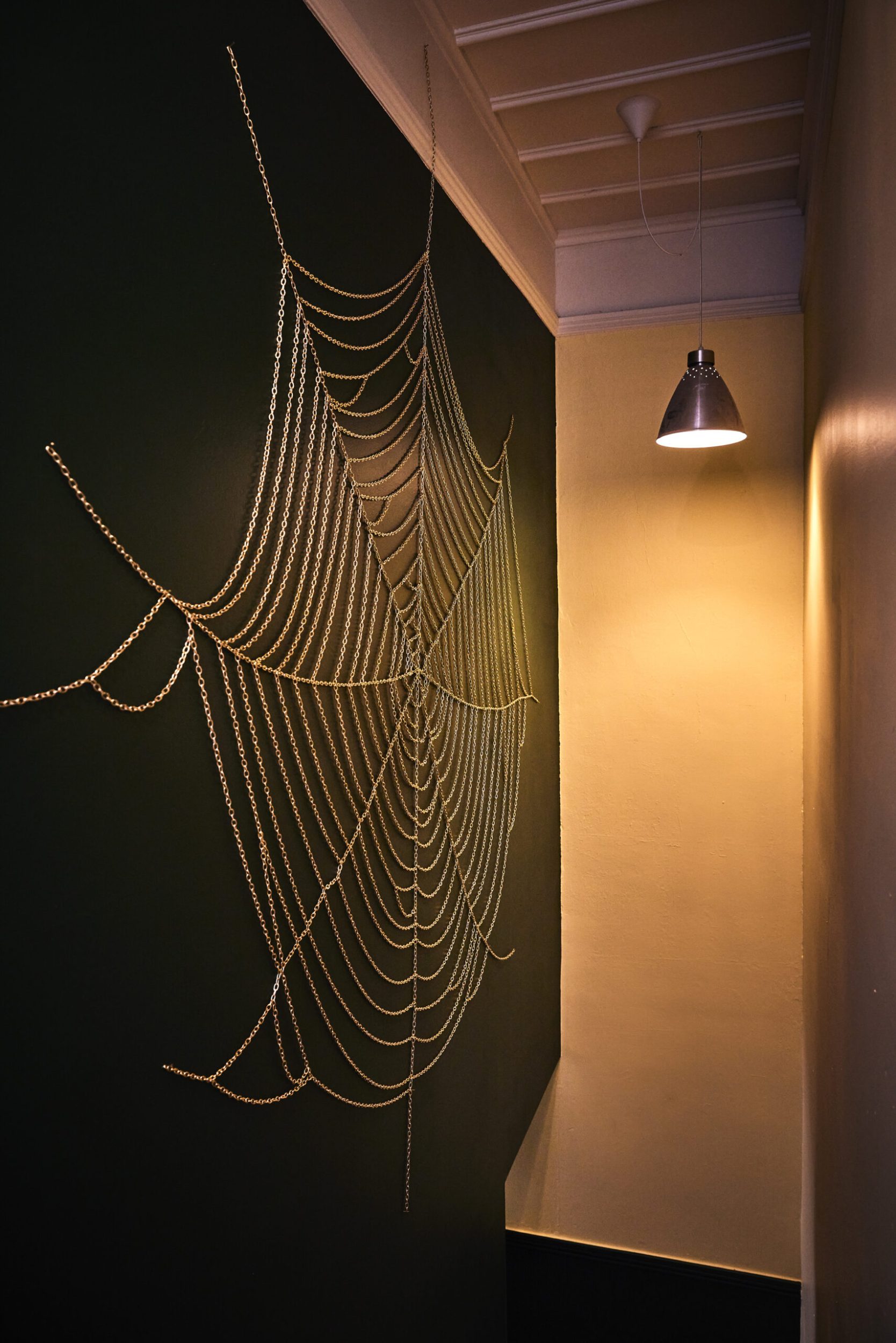 A black wall with a cobweb artwork made out of a gold chain