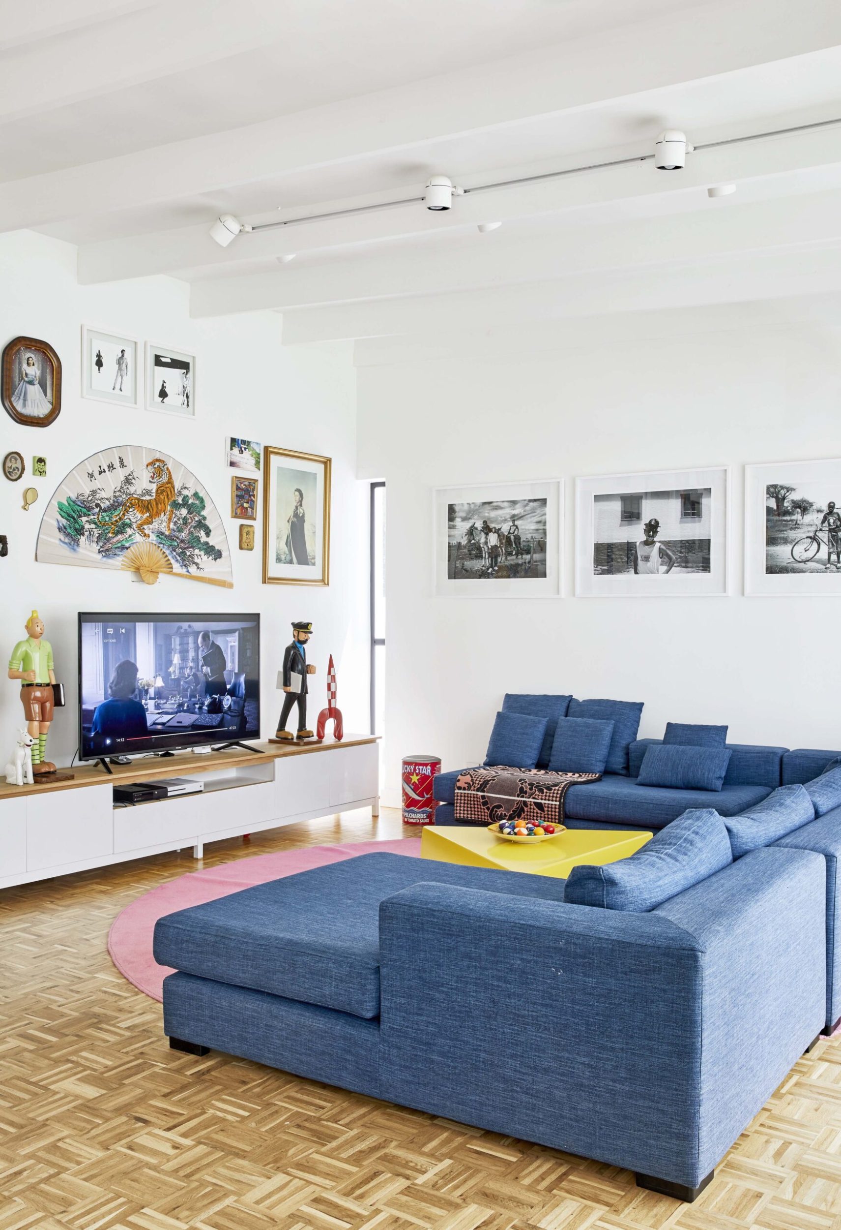 Living room with white walls, wood floors and a large blue couch and assorted hanging wall art 