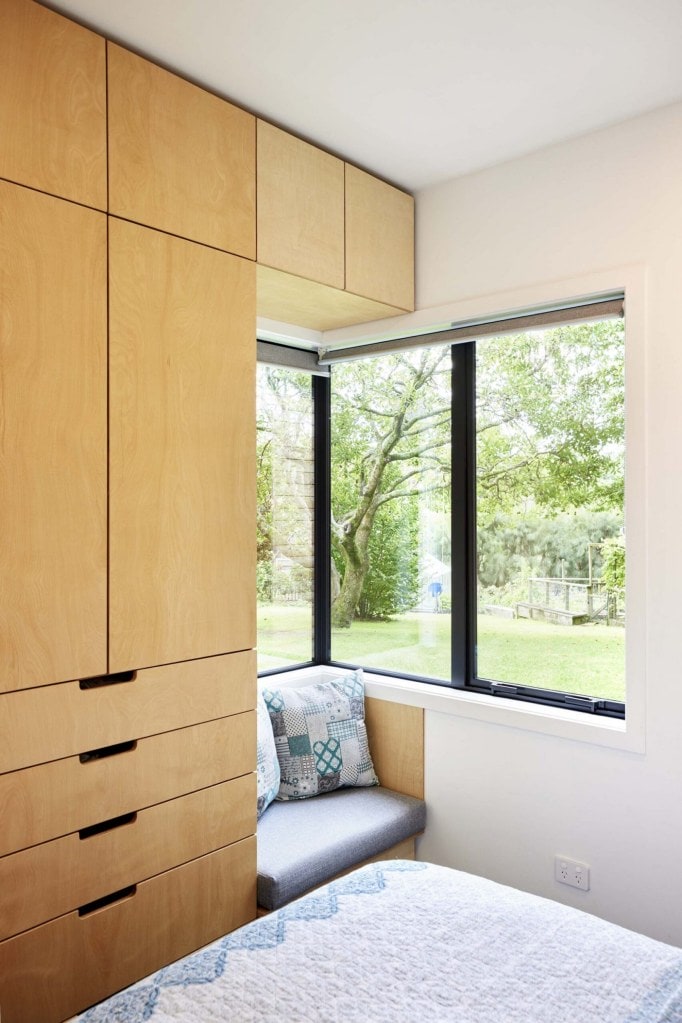 A bedroom with a large corner window and a wood cabinet with multiple drawers