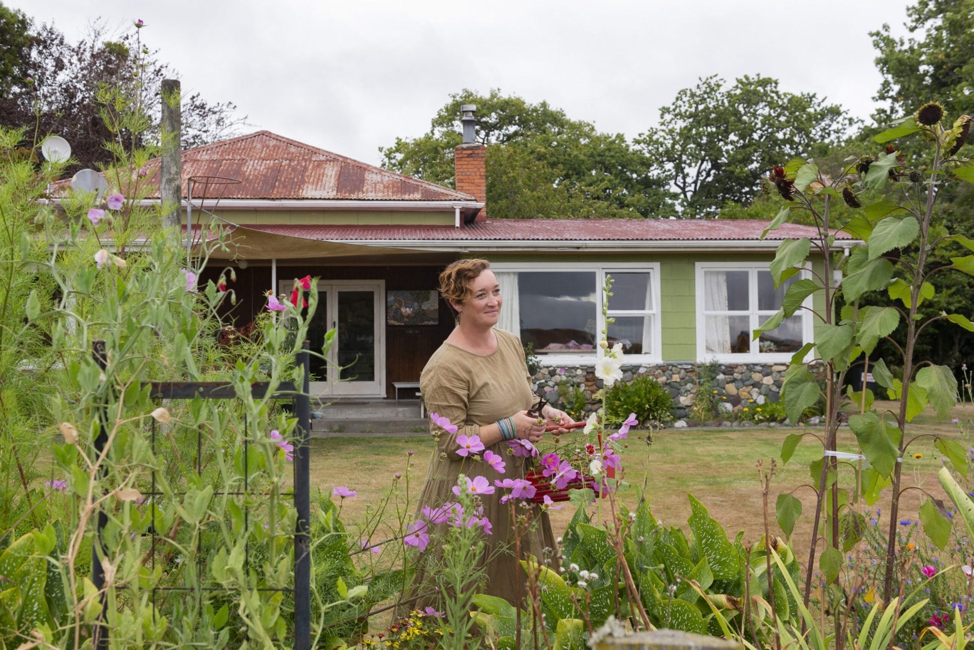 Fleur Woods wearing long green dress standing in garden behind pink flowers