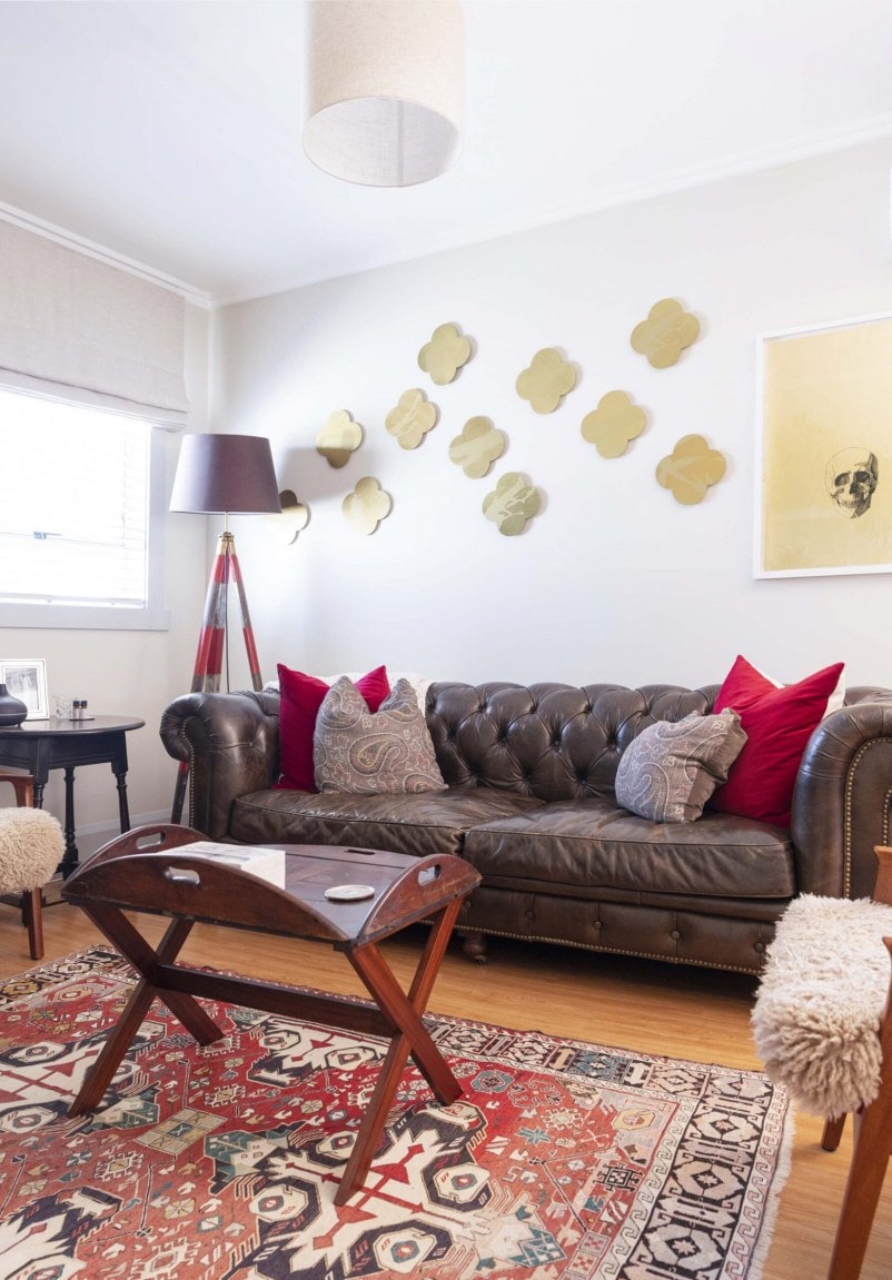 A living room with a brown leather couch, red vintage carpet and butler's tray as a table